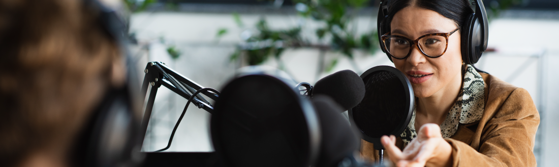 Image shows two people talking into microphones while wearing headphones